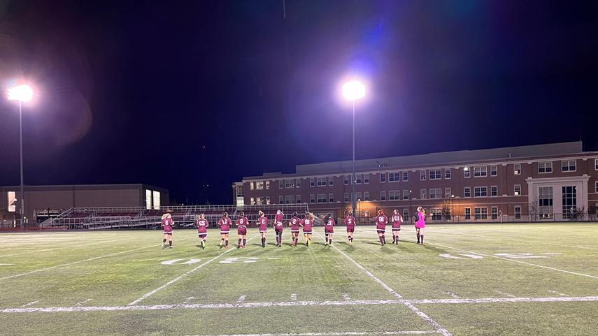 women's soccer team running out into field lit up by lights at night